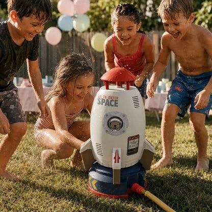 Four children gathered around the rocket water sprinkler at a backyard birthday party, reloading it for another launch