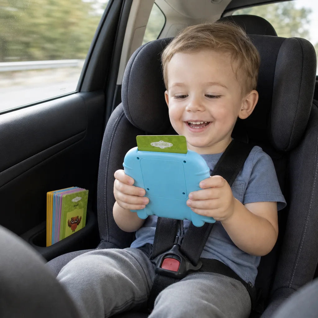 Smiling toddler in a car seat holding the blue talking flash card reader with a card in the top, spare cards tucked in the door pocket