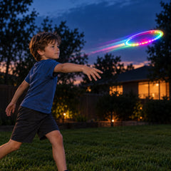 Boy in a dusk garden following through on a backhand throw as the lit disc flies ahead of him