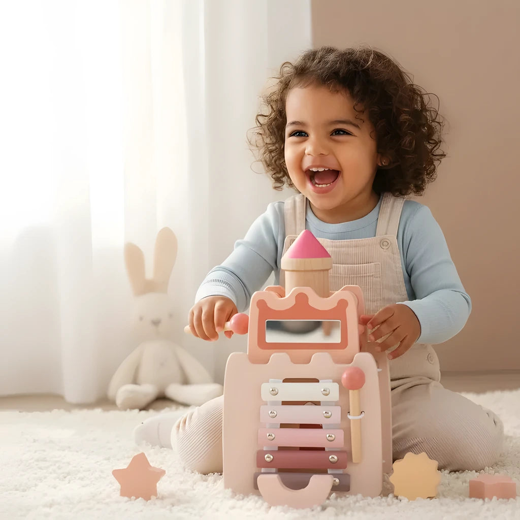 Toddler laughing as she plays the learning castle xylophone, shape pieces on the rug beside her