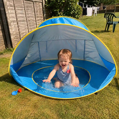 Toddler splashing in the shaded paddling pool of the Little Cubs pop up pool tent on a back garden lawn