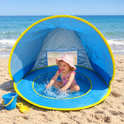 Toddler splashing in the shaded pool of the Little Cubs pop up beach tent on golden sand by the sea