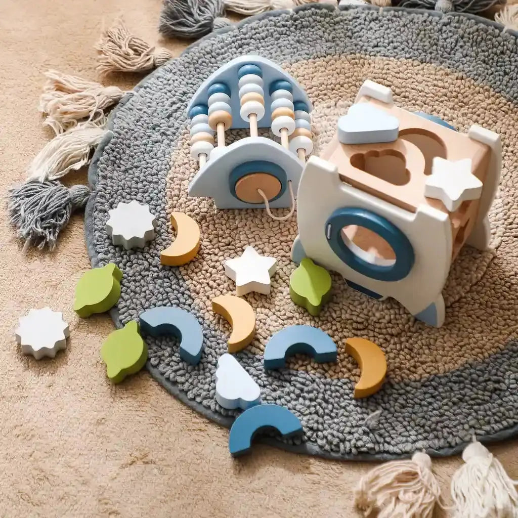 The wooden learning rocket on a rug with all its star, moon, cloud, leaf, arch and flower shape pieces laid out