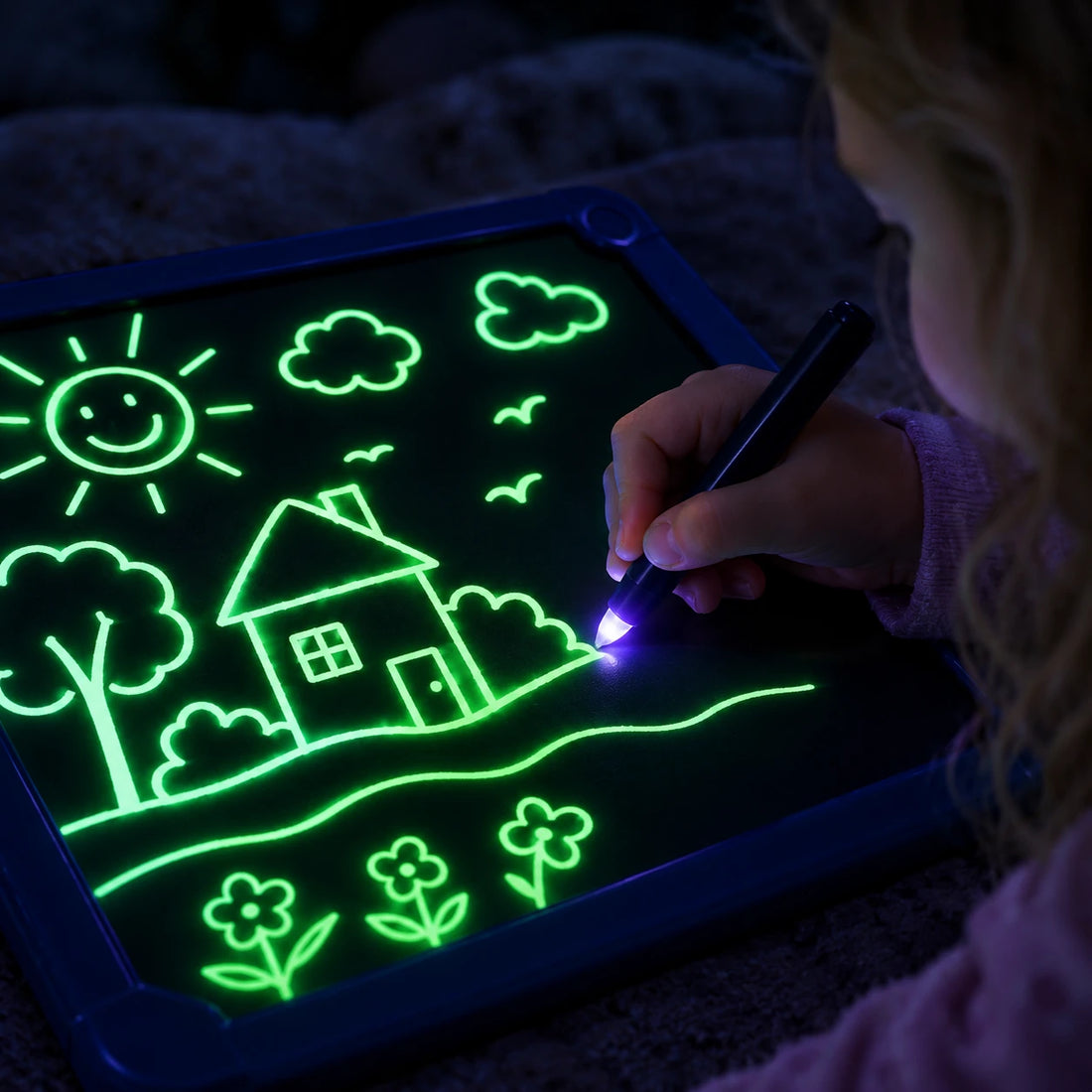 Child's hand drawing a glowing neon green line on the dark board with the light pen